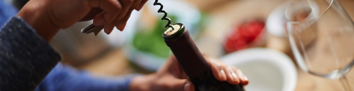 Une personne ouvre une bouteille de vin rouge avec un tire-bouchon à table