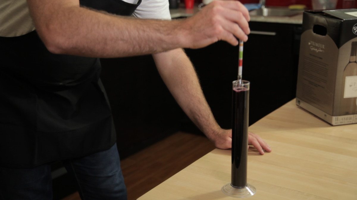 Un vinificateur mesure la densité du vin rouge en plongeant un hydromètre dans une éprouvette