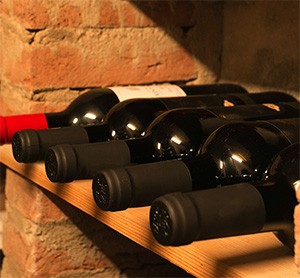 Bouteilles de vin couchées sur une tablette en bois contre un mur de briques, dans une cave