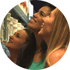 Trois femmes souriantes regardent les tablettes de produits de vinification d'un magasin