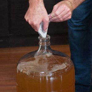 Mains qui versent un sachet de clarifiant dans le goulot d'une tourie de vin trouble