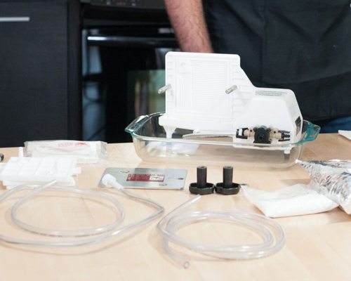 Pièces d'un filtre à plaques Buon Vino sur un comptoir : l'appareil dans un plat en verre, tampons filtrants, tubes et raccords