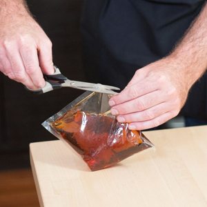 Mains qui ouvrent aux ciseaux un sachet de mélange édulcorant ambré sur un comptoir de bois