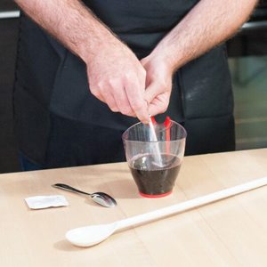 Mains qui dissolvent le contenu d'un sachet dans une tasse à mesurer de vin, le sachet vide et une longue cuillère à côté