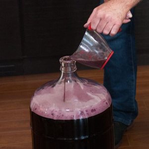 Vin versé d'une tasse à mesurer dans le goulot d'une tourie, formant une mousse rose