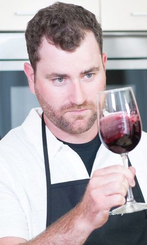 Un vinificateur en tablier incline un verre de vin rouge vers la lumière pour en juger la couleur et la limpidité