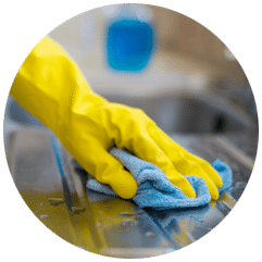 Une main gantée de jaune essuie un comptoir en acier inoxydable avec un chiffon en microfibre bleu