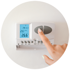 Un doigt appuie sur un thermostat mural réglé à 23 degrés, qui affiche 26,6 degrés