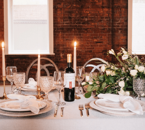 Bottle of red wine on a candlelit wedding place setting with white roses and gold cutlery