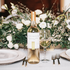 Bottle of En Primeur white wine beside a filled glass on a wedding table of white roses and gold cutlery