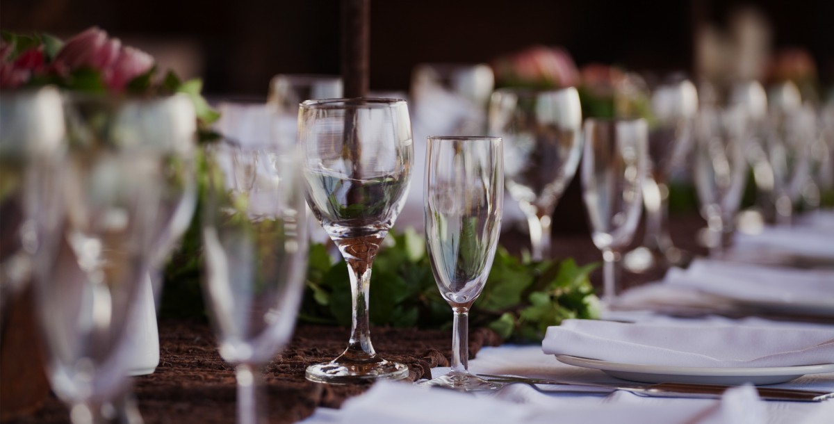Longue table de banquet dressée avec des verres à vin, des serviettes blanches et des centres de table fleuris