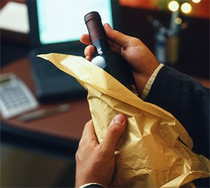 Mains qui déballent une bouteille de vin de son papier de soie doré, à un bureau