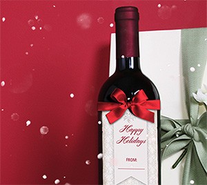 Bouteille de vin rouge ornée d'un nœud rouge et d'une étiquette-cadeau « Happy Holidays », à côté d'un cadeau emballé