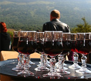 Plateau de verres de vin rouge sur une table surplombant une vallée boisée, un homme assis à l'arrière