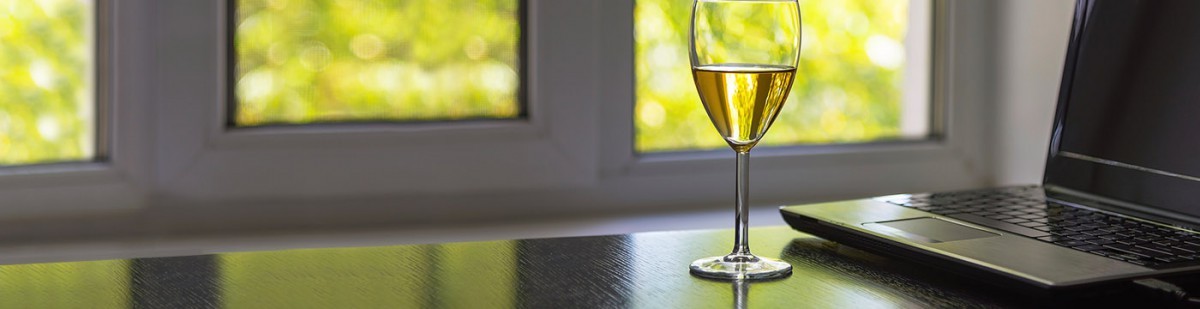 Glass of white wine on a table beside an open laptop, ready for watching winemaking videos
