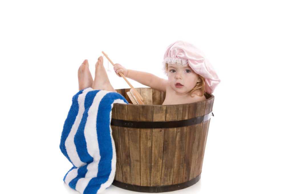 A cute two year old girl having a bath in a wooden barrel tub. Isolated on white.