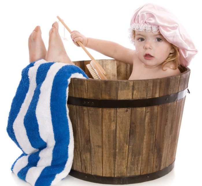 A cute two year old girl having a bath in a wooden barrel tub. Isolated on white.