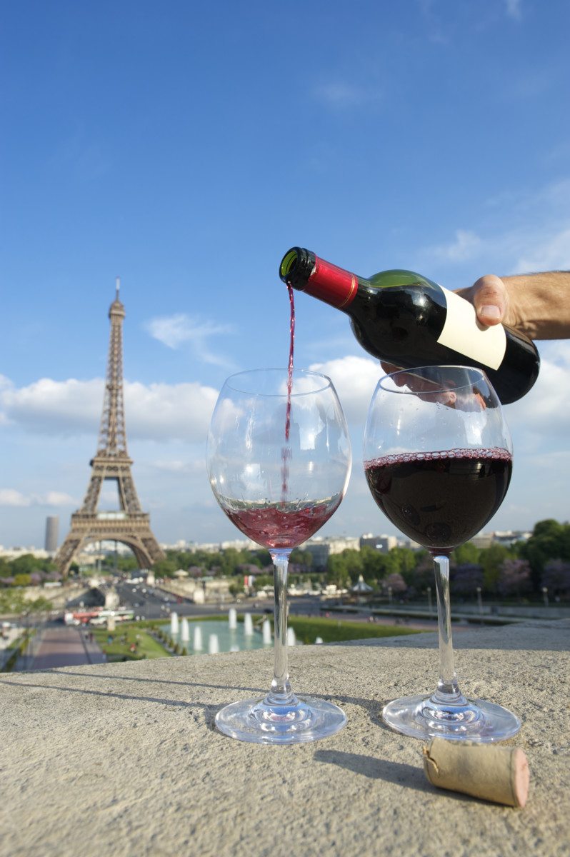 Hand pouring red wine from bottle into glasses in front of romantic view of Eiffel Tower in Paris France