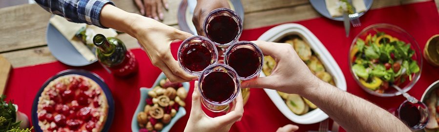 Group of friends toasting with glasses of red wine by festive table